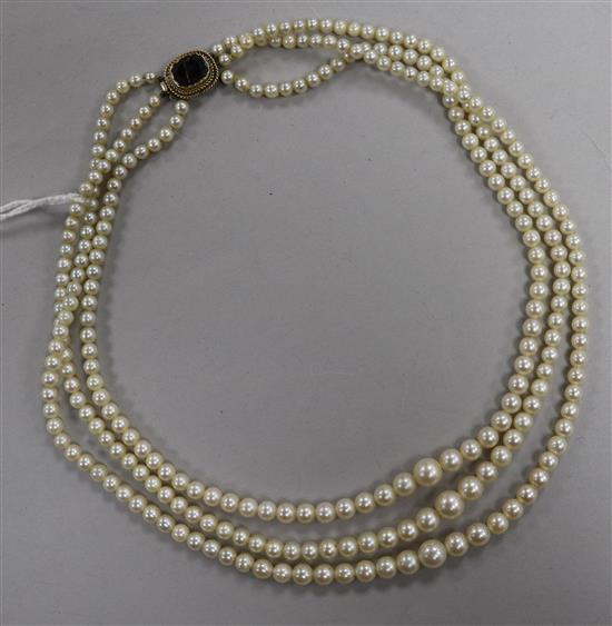 A triple strand graduated cultured pearl necklace with yellow metal and garnet set clasp, 38cm.